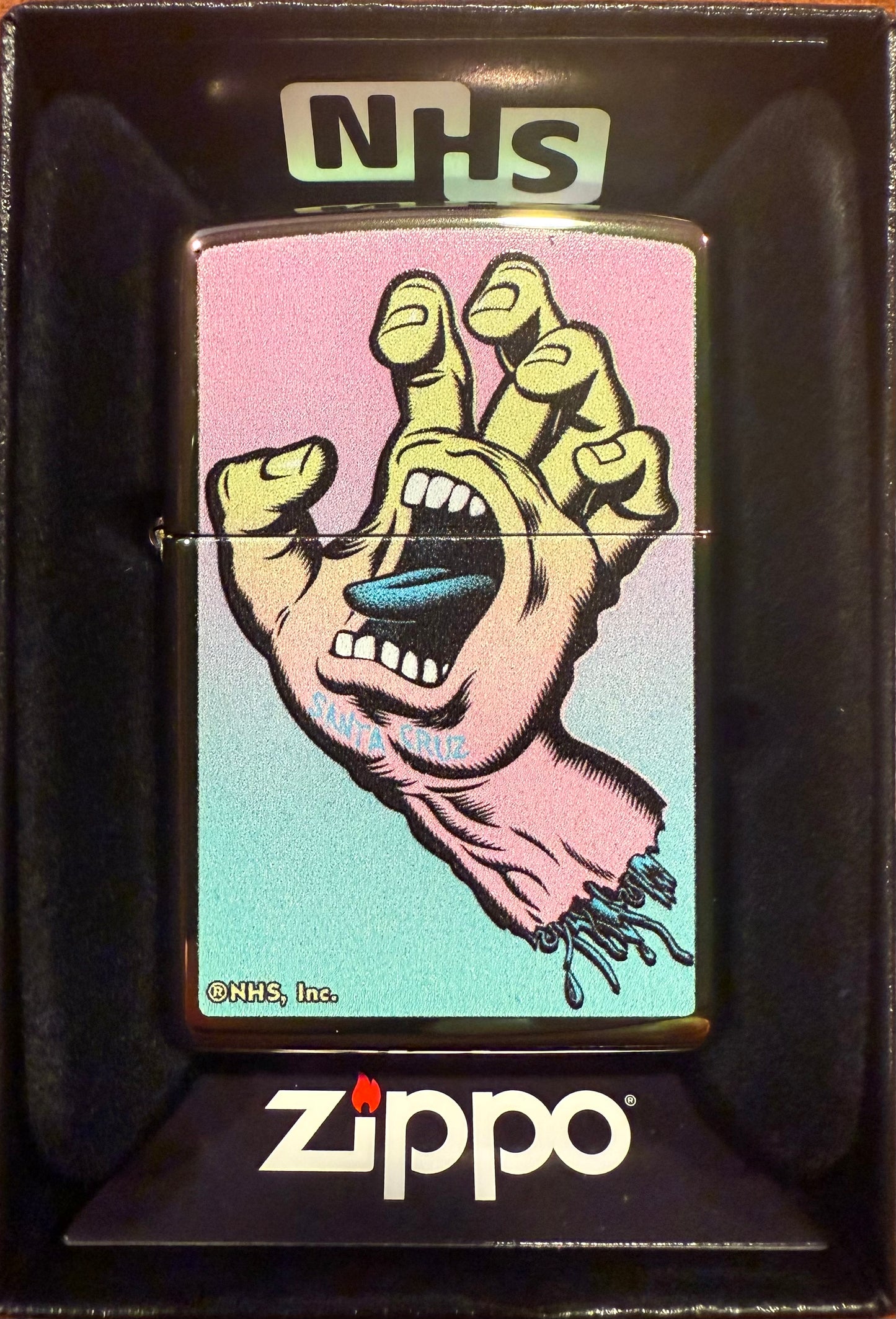 A Zippo lighter with the Santa Cruz Screaming Hand artwork in a color imaged Spectraflame finish, displayed in its packaging.