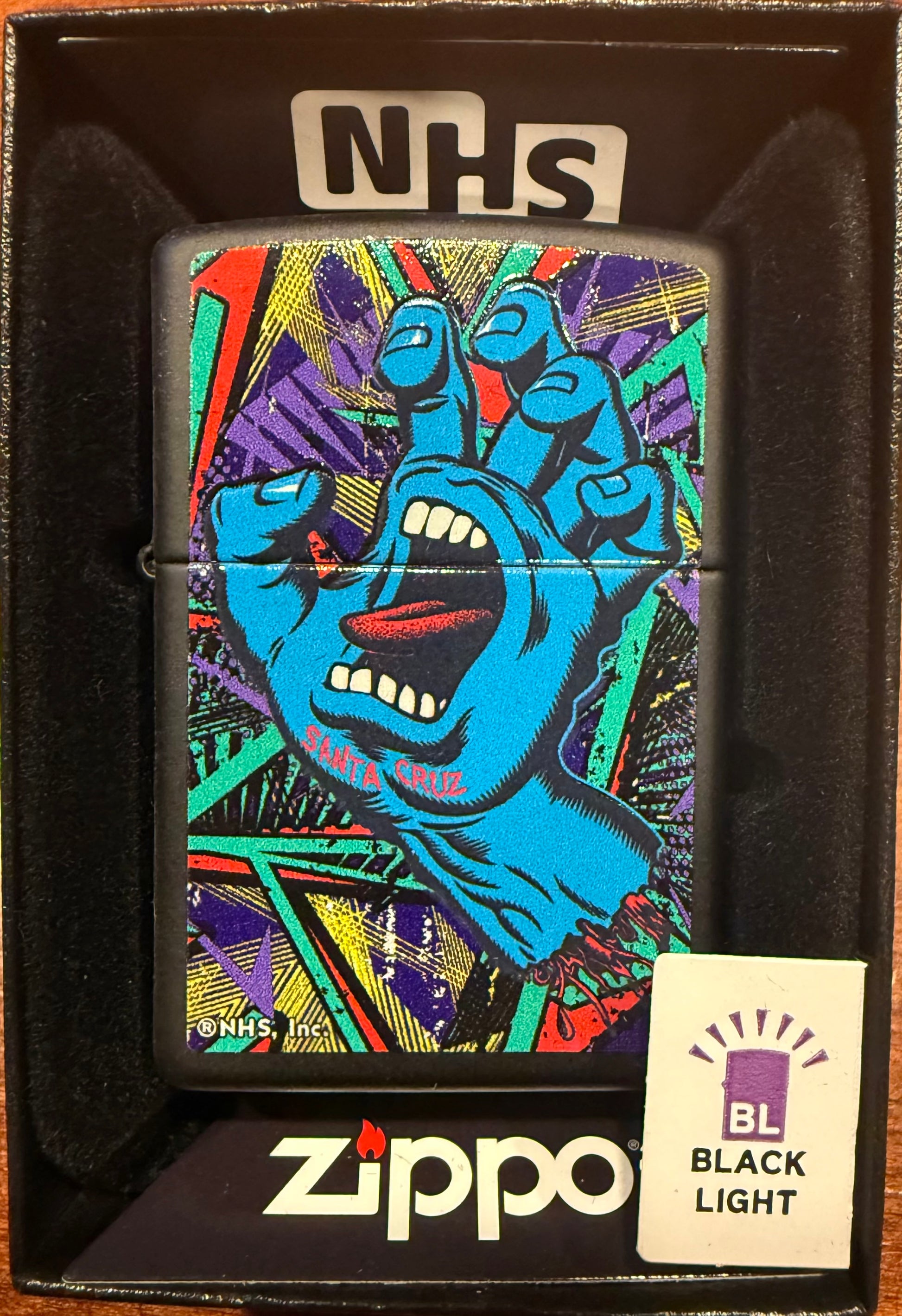 A Zippo lighter with a vibrant multicolored hand design, packaged in a black box with 'NHS' and 'Blacklight' text.