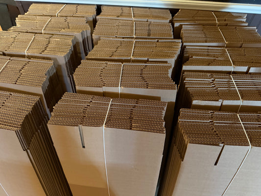 A stack of cardboard boxes designed to ship skateboard decks, showing the boxes' folded edges and the brown paper interiors.