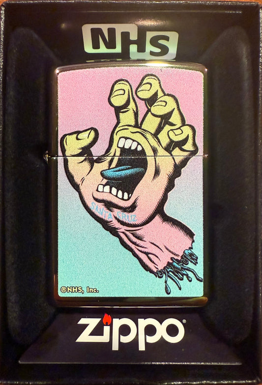 A Zippo lighter with the Santa Cruz Screaming Hand artwork in a color imaged Spectraflame finish, displayed in its packaging.