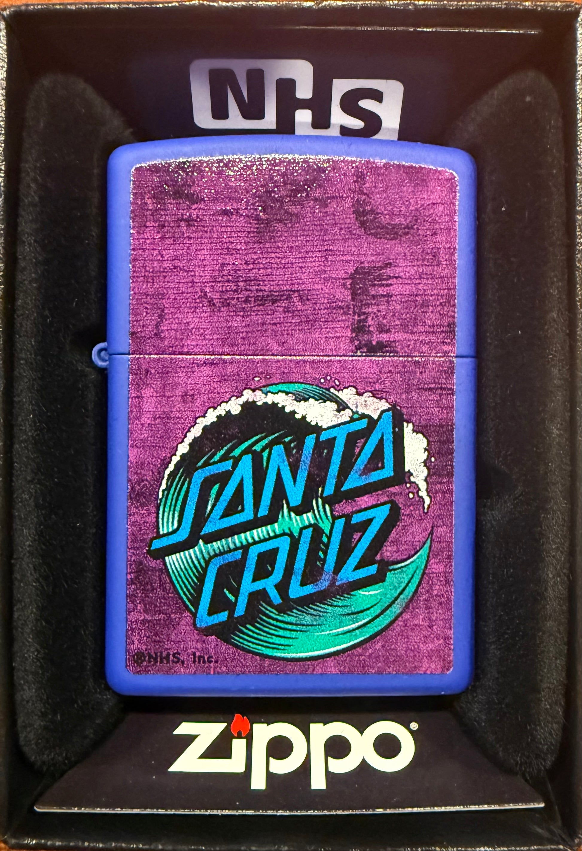A Zippo lighter with a blue background featuring the Santa Cruz Skateboards iconic wave graphic, presented in a gift box with the Zippo logo.